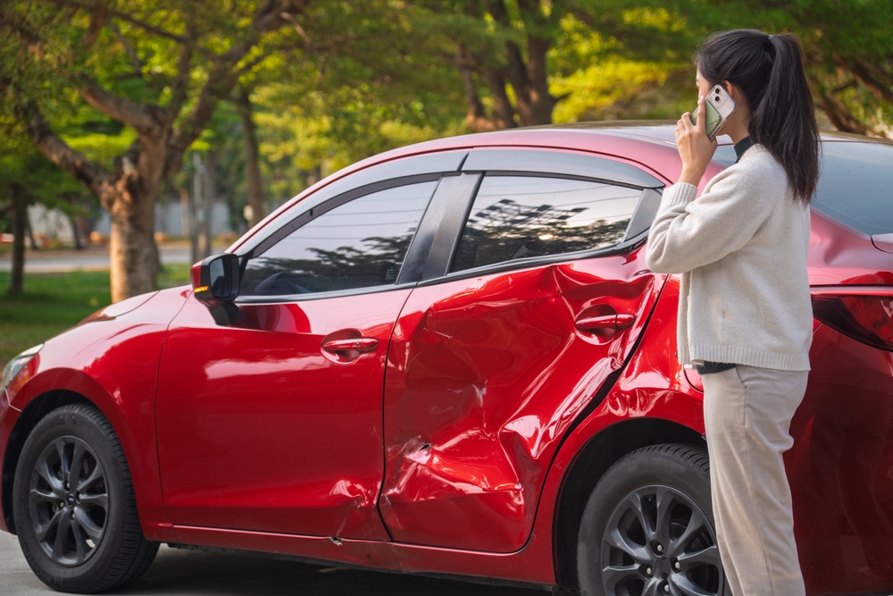 Photo of a dented red car and a woman on the phone, highlighting the importance of calling a lawyer after a car accident in New Jersey to preserve your rights. 